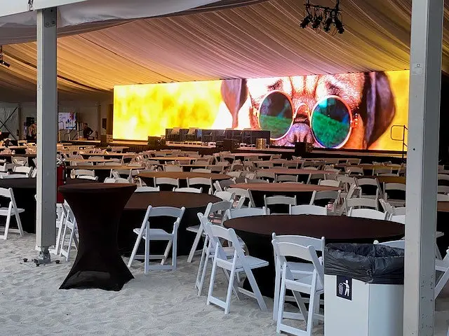 Beachfront event tent with seating and a large presentation display